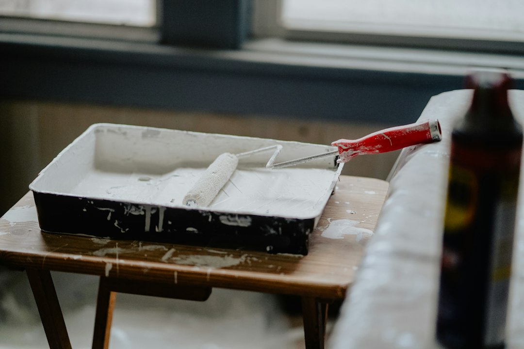 A paint roller with a red handle in a tray of white paint in Riverside, CA